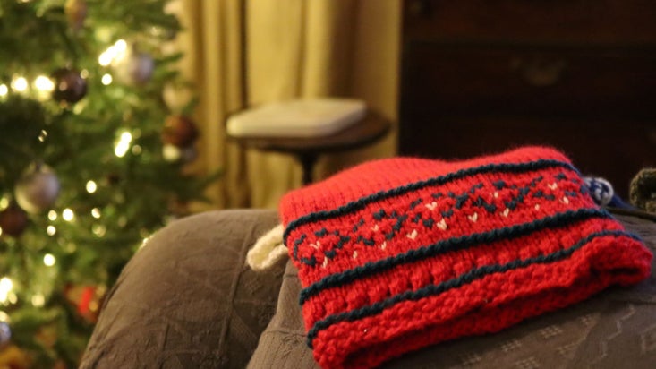 Knitted stocking hangs over the edge of a sofa with a lit Christmas tree twinkling in the background.